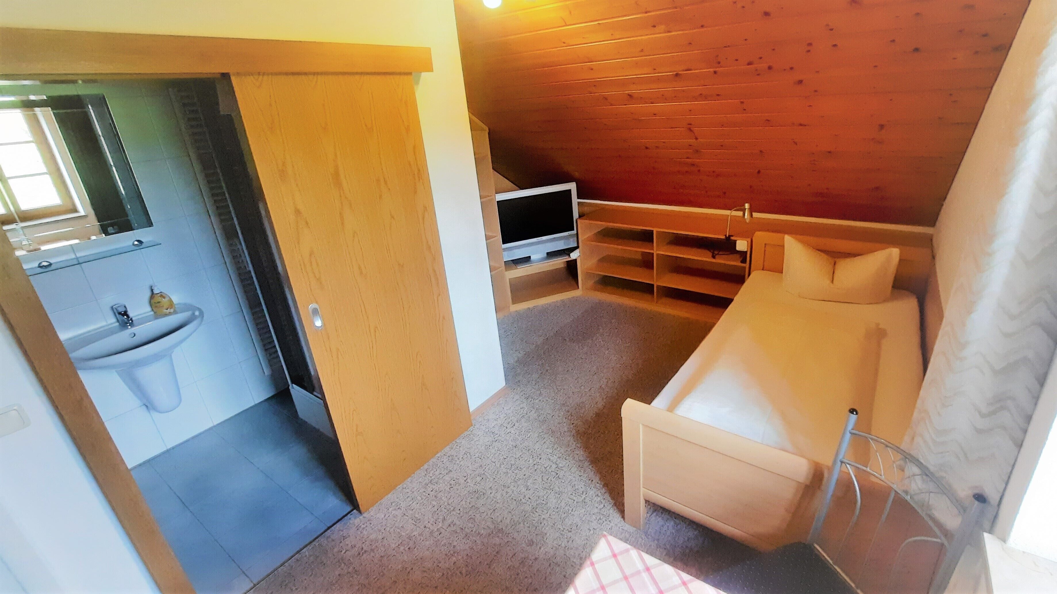 A small, cozy room with a bed, a TV, and a bathroom with a sink.