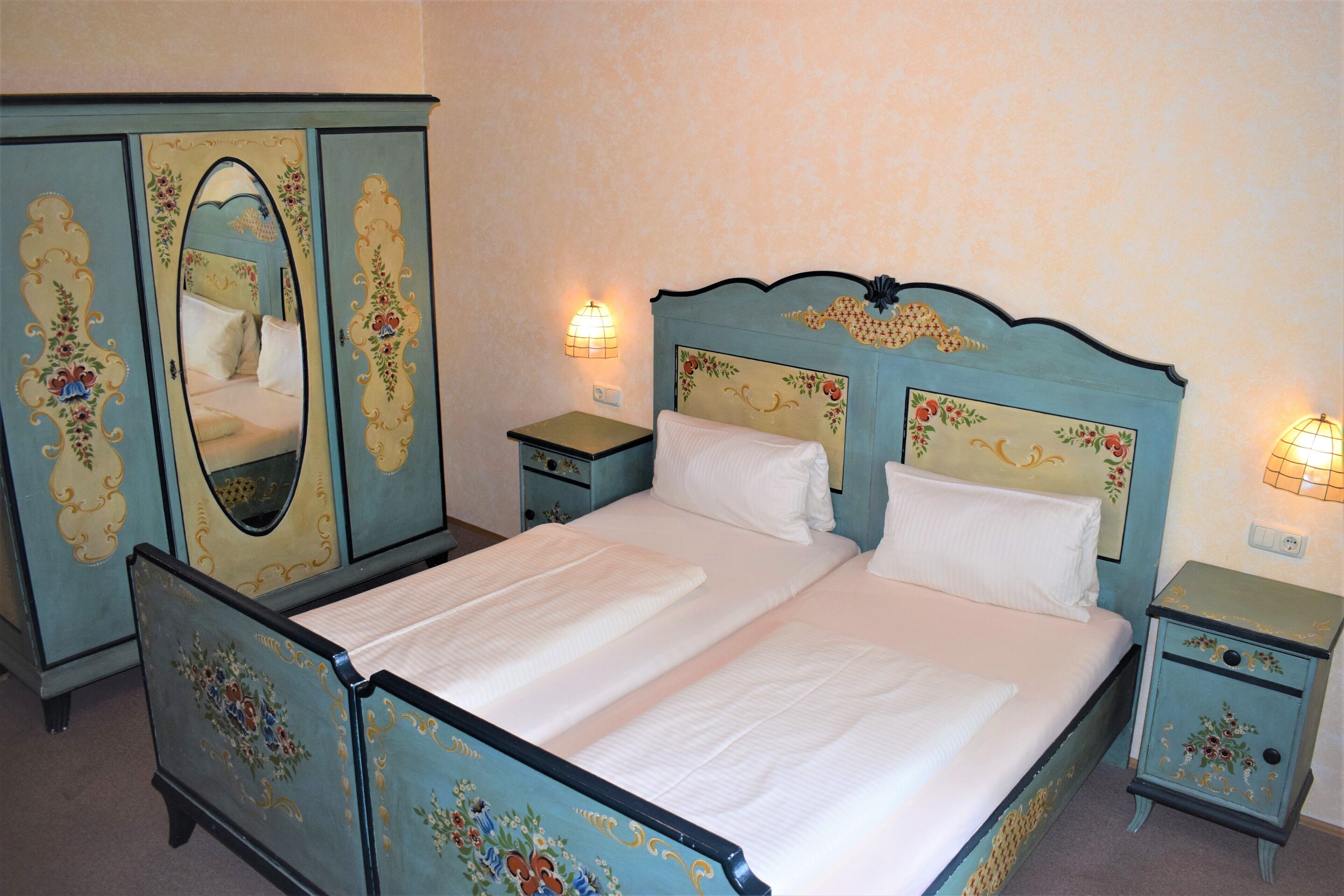 A bedroom with a bed, two nightstands, a dresser with a mirror, and floral wall decorations.
