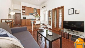 Una sala moderna con sofá, mesa de centro, televisión y cocina al fondo.