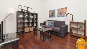Una sala de estar moderna con un sofá gris, una estantería negra, una mesa de centro y un televisor sobre un mueble.