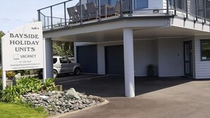 Un edificio de dos pisos con un balcón, un letrero que indica 'Bayside Holiday Units' y 'Disponibilidad', y un número de contacto.