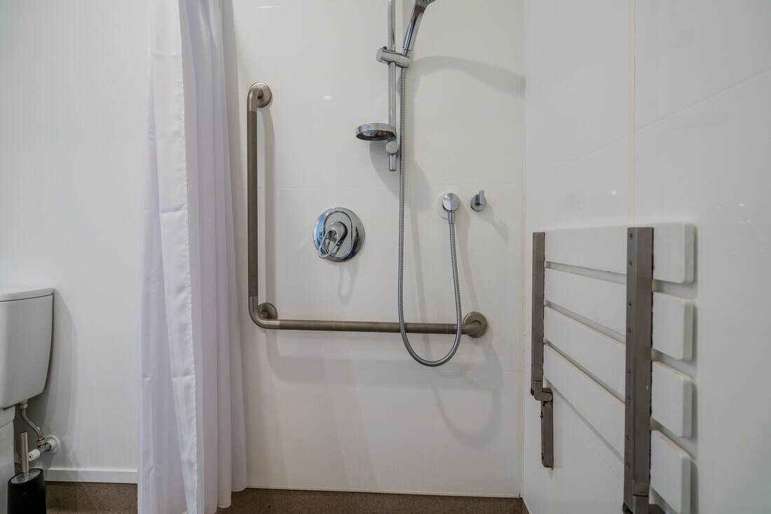 Ein Badezimmer mit Dusche, Haltegriffen und Toilette.