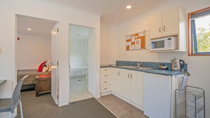 Cocina compacta con armarios blancos, microondas y tetera. Hay un pequeño comedor con una silla y una mesa.