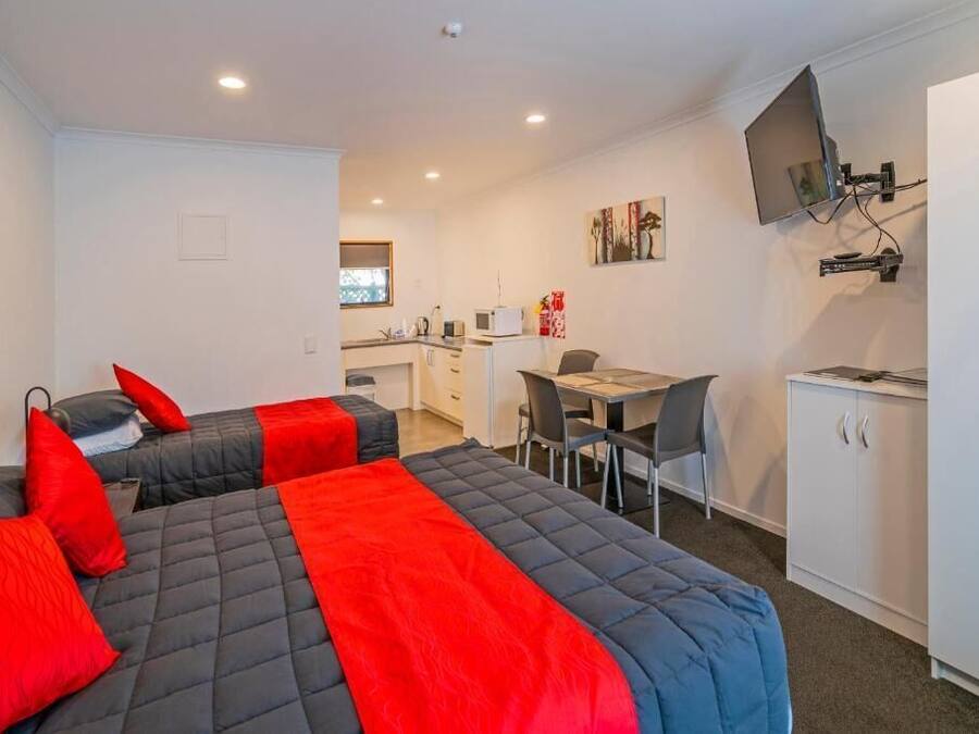 Une chambre d’hôtel compacte comprenant deux lits, une kitchenette, un coin repas et un téléviseur fixé au mur.