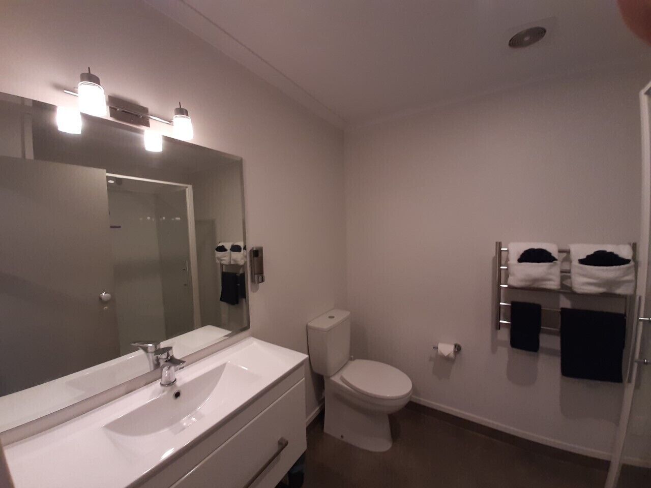 Een badkamer met een witte wastafel, spiegel en toilet. Handdoeken hangen aan een rek.