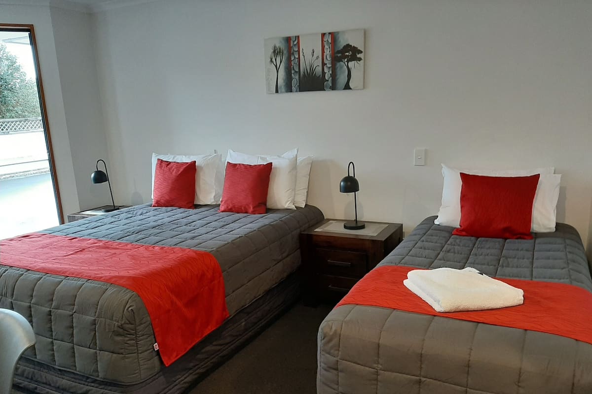 A hotel room with two beds, each with a red and grey quilted bedspread, white pillows, and a nightstand with a lamp.