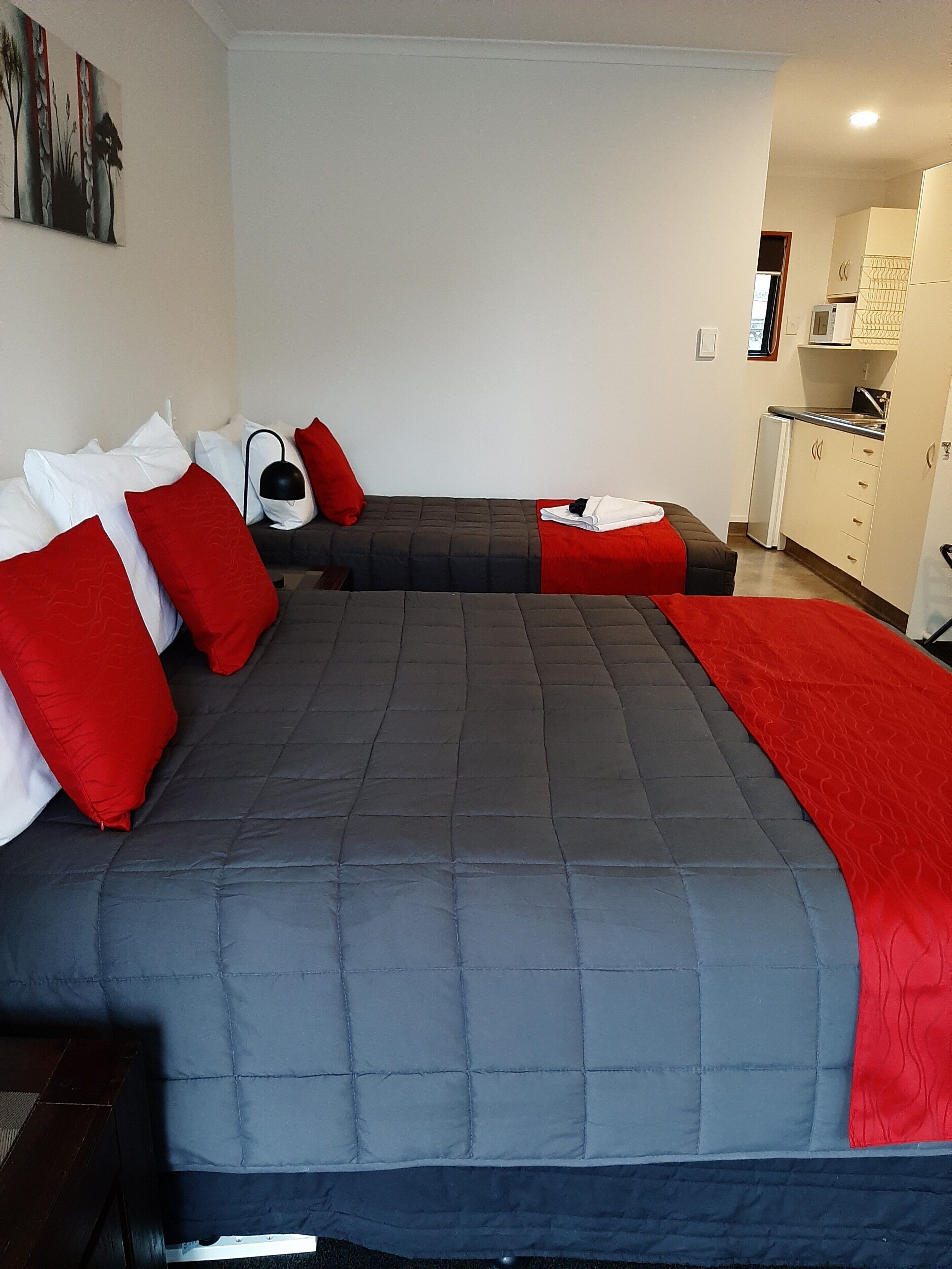 Een tweepersoonsbed met rode en witte kussens, een grijze deken en een rode plaid.