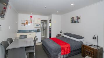 A compact hotel room with a bed, bedside table, desk, and chairs.