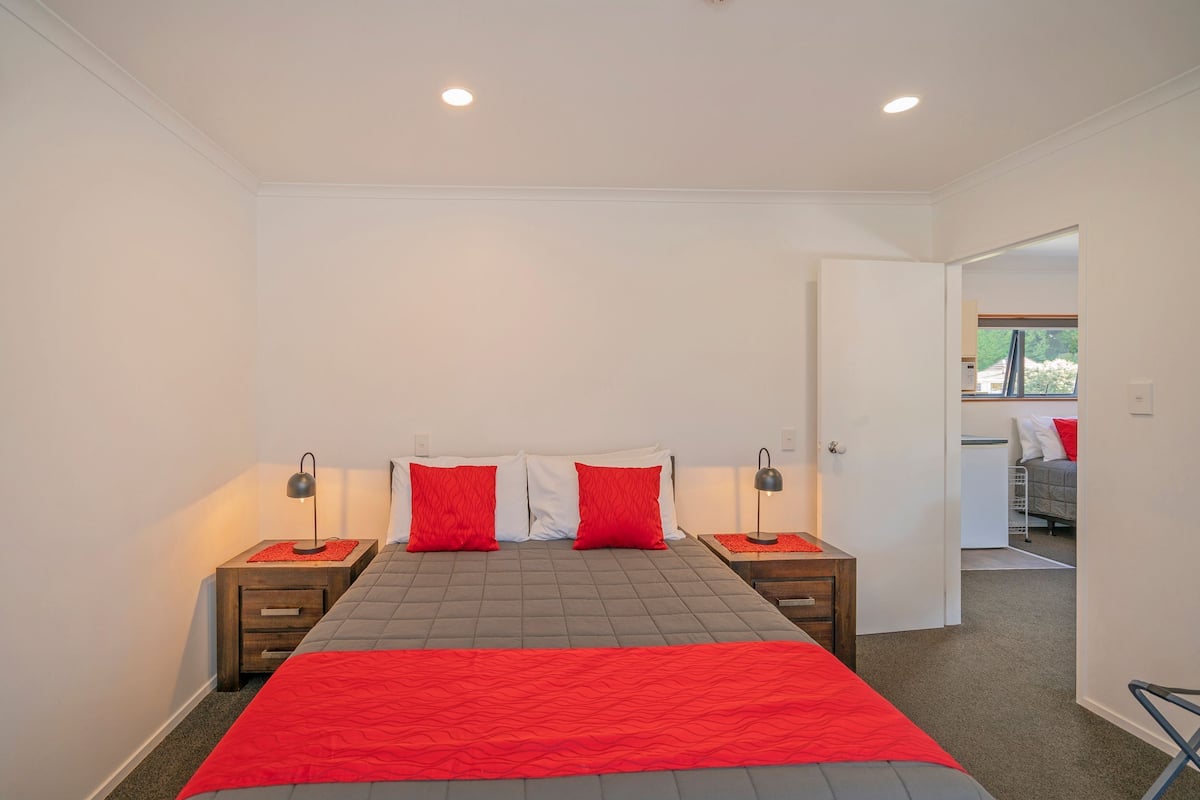 A bedroom with a bed, two nightstands, and a door leading to another room.