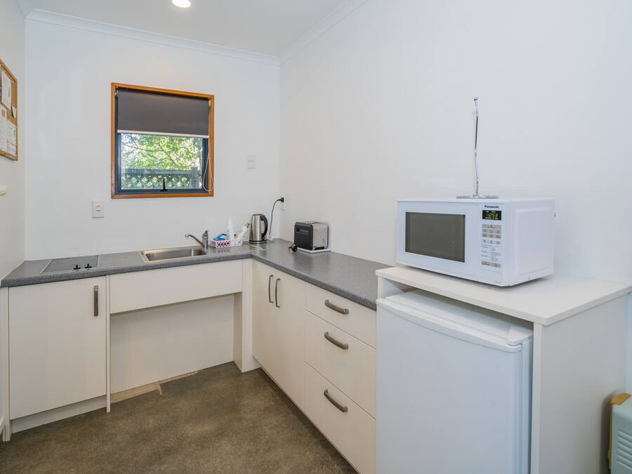 A compact kitchen with white cabinets, a sink, a microwave, and a small refrigerator.