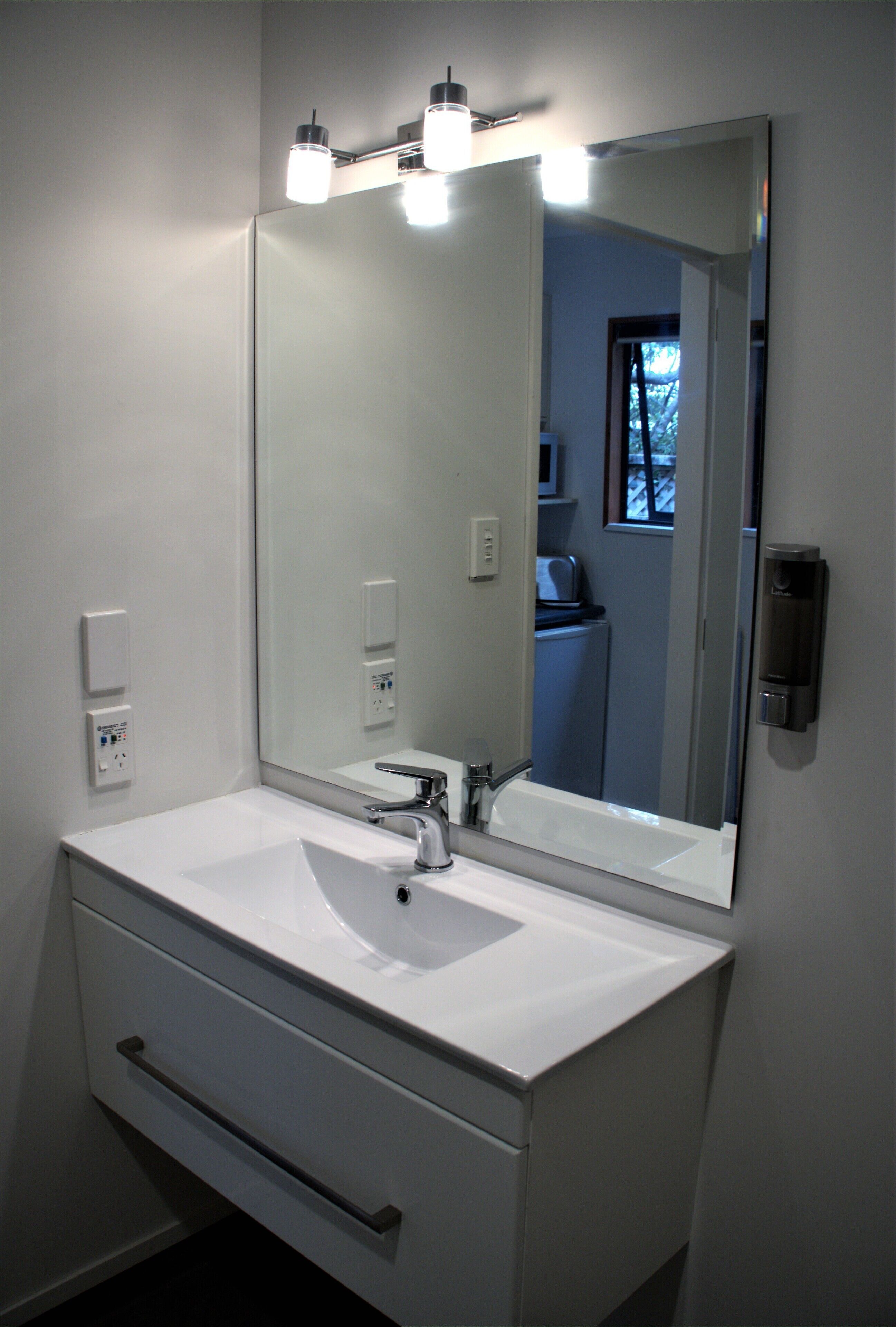 Un baño moderno con un lavamanos blanco, un espejo grande e iluminación en el techo.