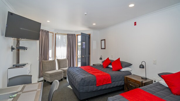Habitación de hotel con cama, escritorio, silla, televisor y ventana con cortinas.