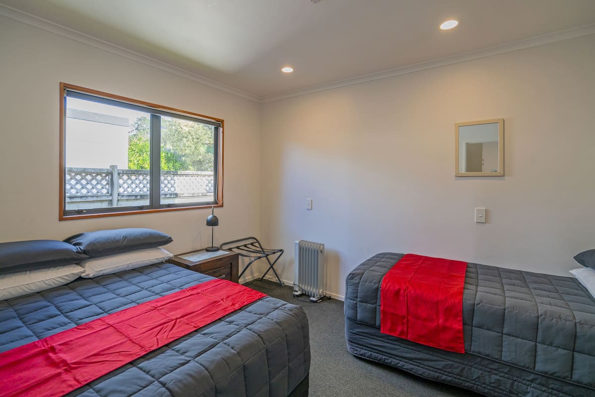 A bedroom with two beds, a window, a radiator, and a mirror.
