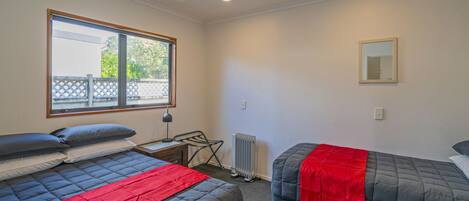 A bedroom with two beds, a window, a radiator, and a mirror.