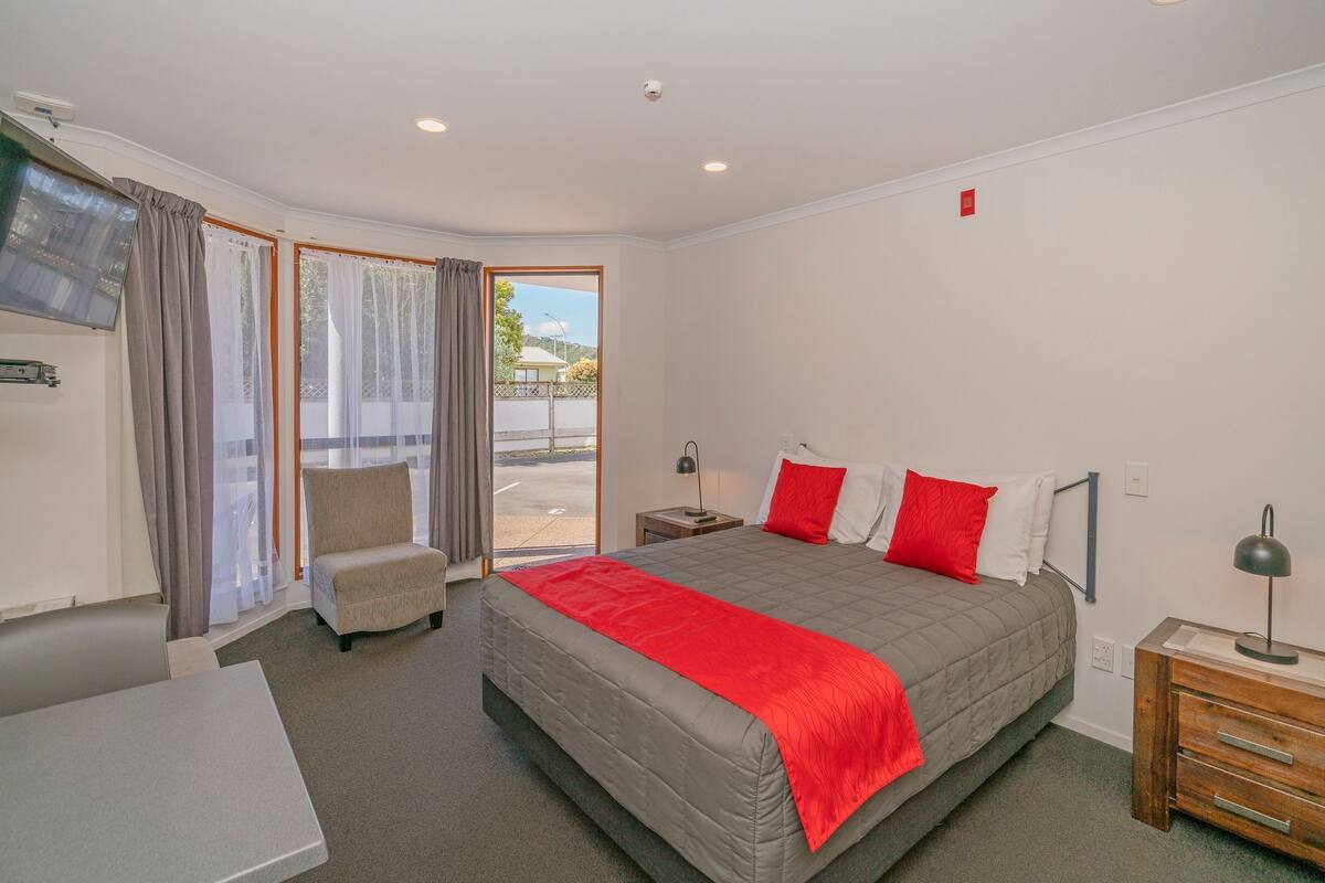 A hotel room with a bed, a chair, a desk, and a view through the door.