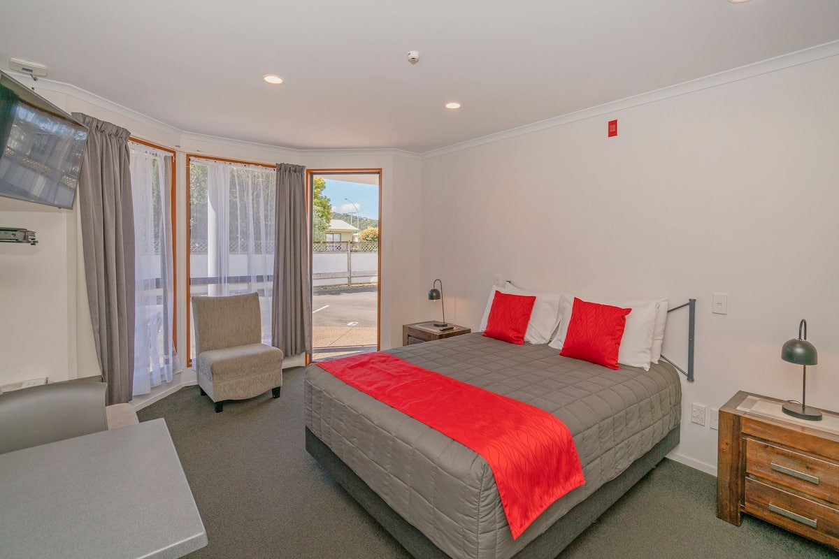 A hotel room with a bed, a chair, a desk, and a view of the outdoors.