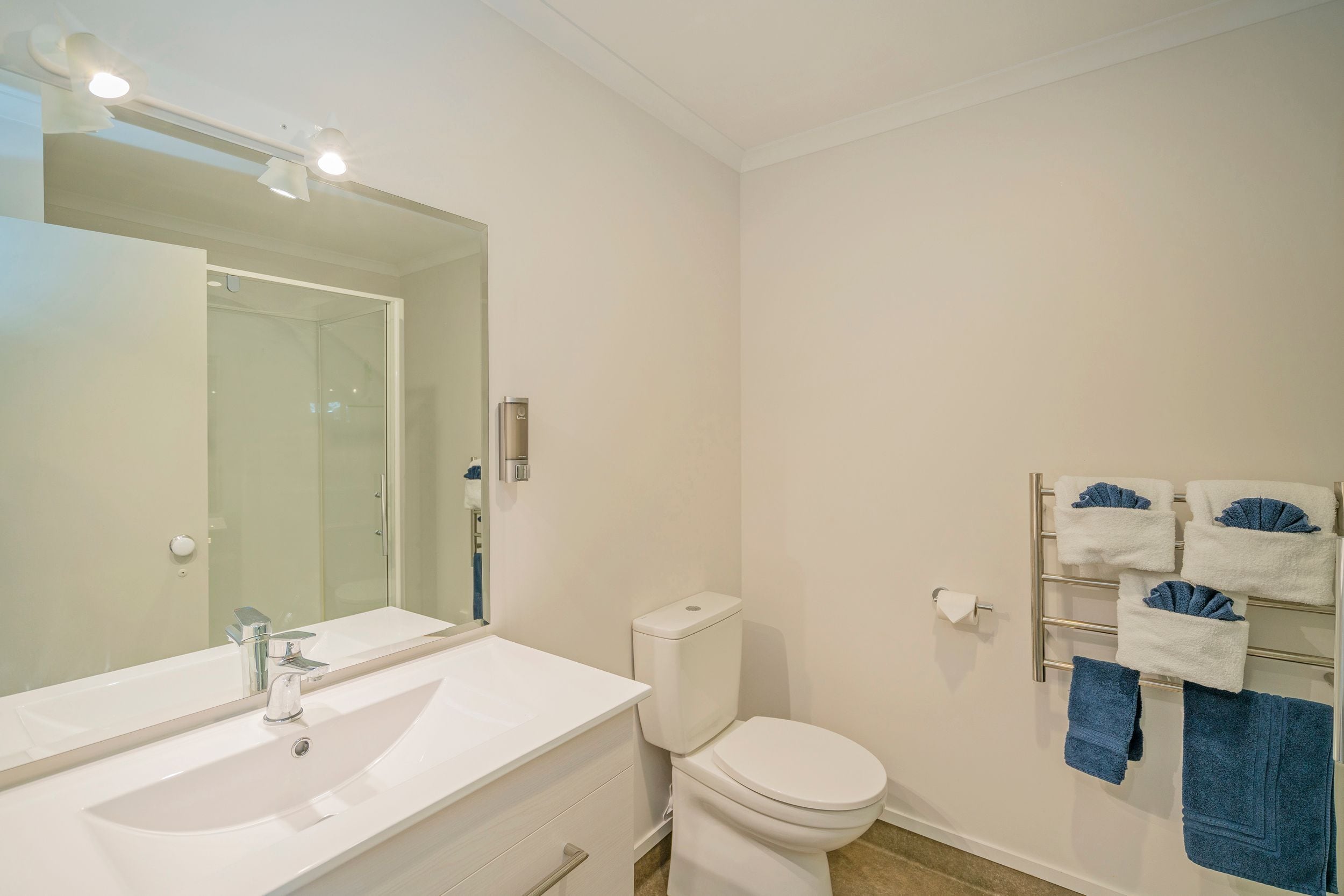 A bathroom with a white sink, a mirror, a toilet, and a towel rack with towels.