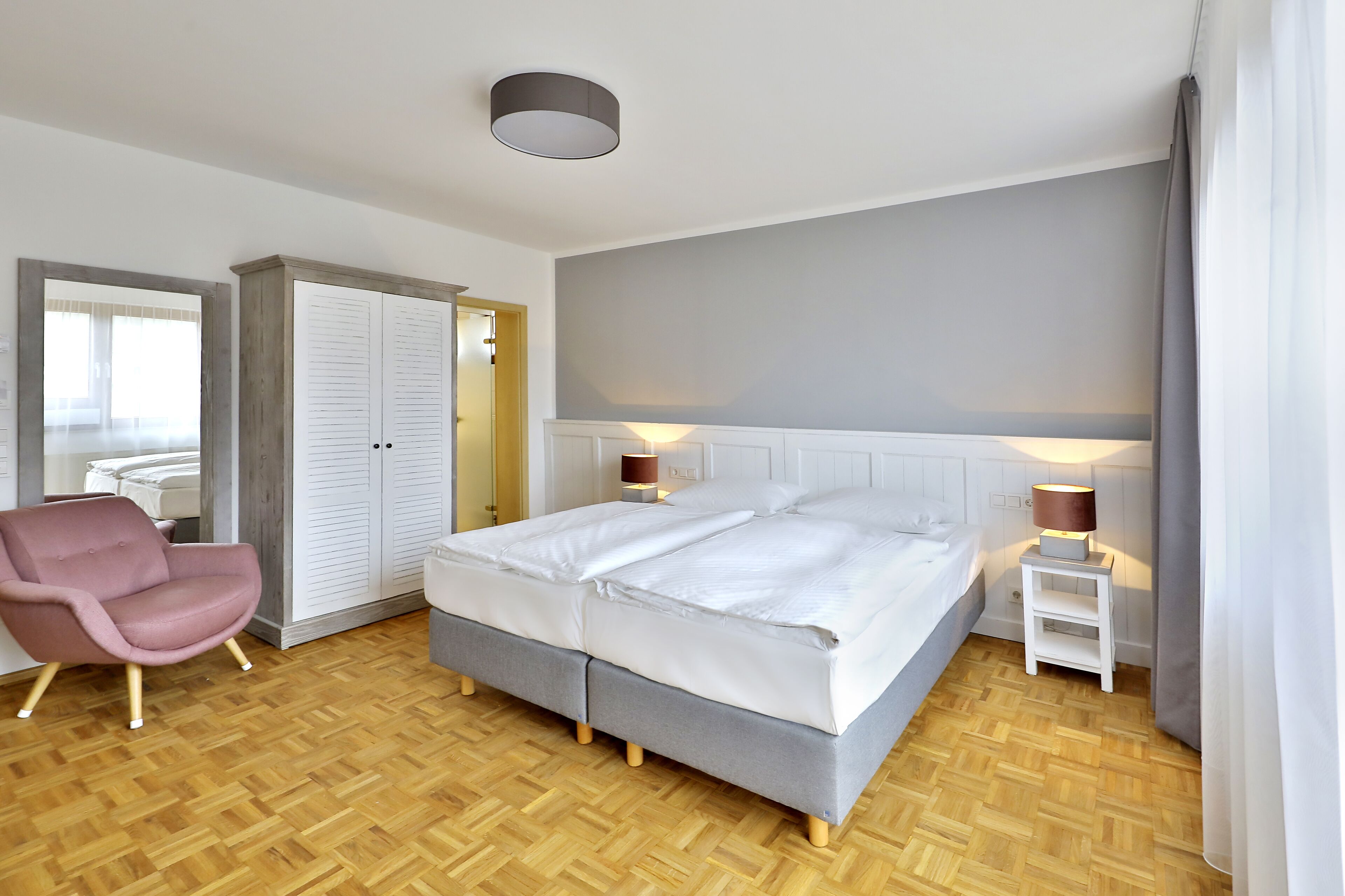 Ein Schlafzimmer mit einem Doppelbett, einem kleinen Nachttisch mit Lampen, einem rosa Sessel und einem Kleiderschrank.