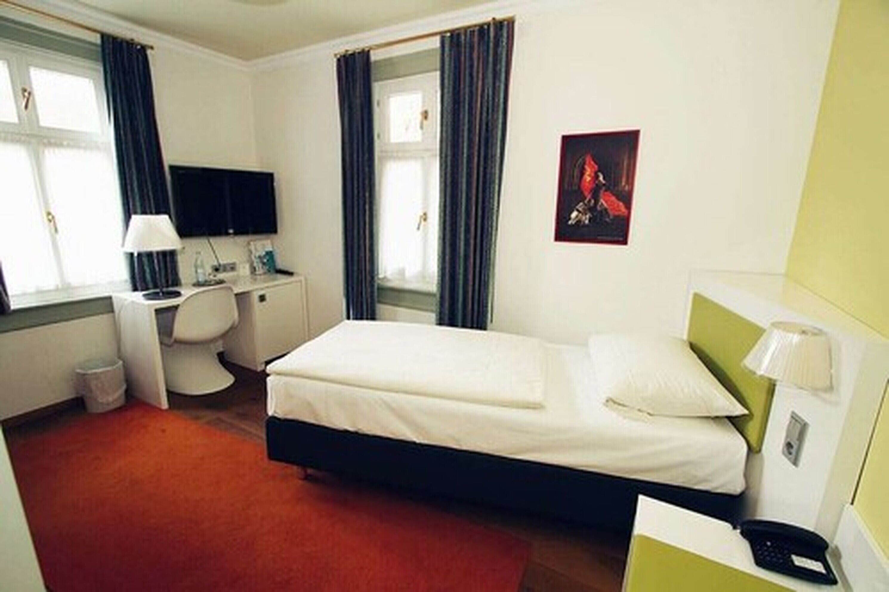 A hotel room with a bed, a desk, a chair, a TV, and a window with curtains.