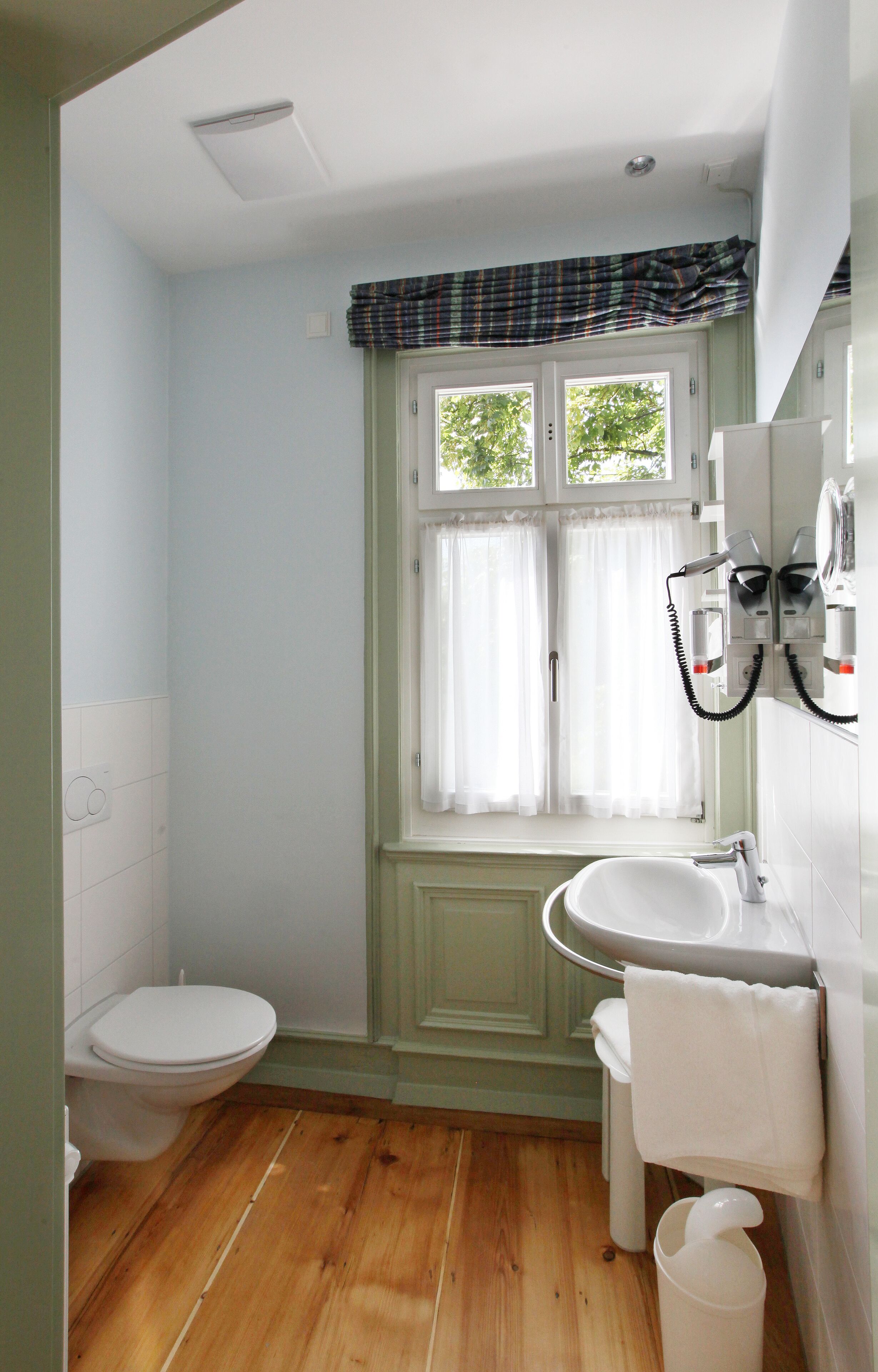 A bathroom with a toilet, sink, and window with curtains.