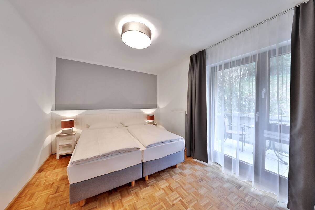 A modern bedroom with a large bed, bedside lamps, and a view of an outdoor patio.