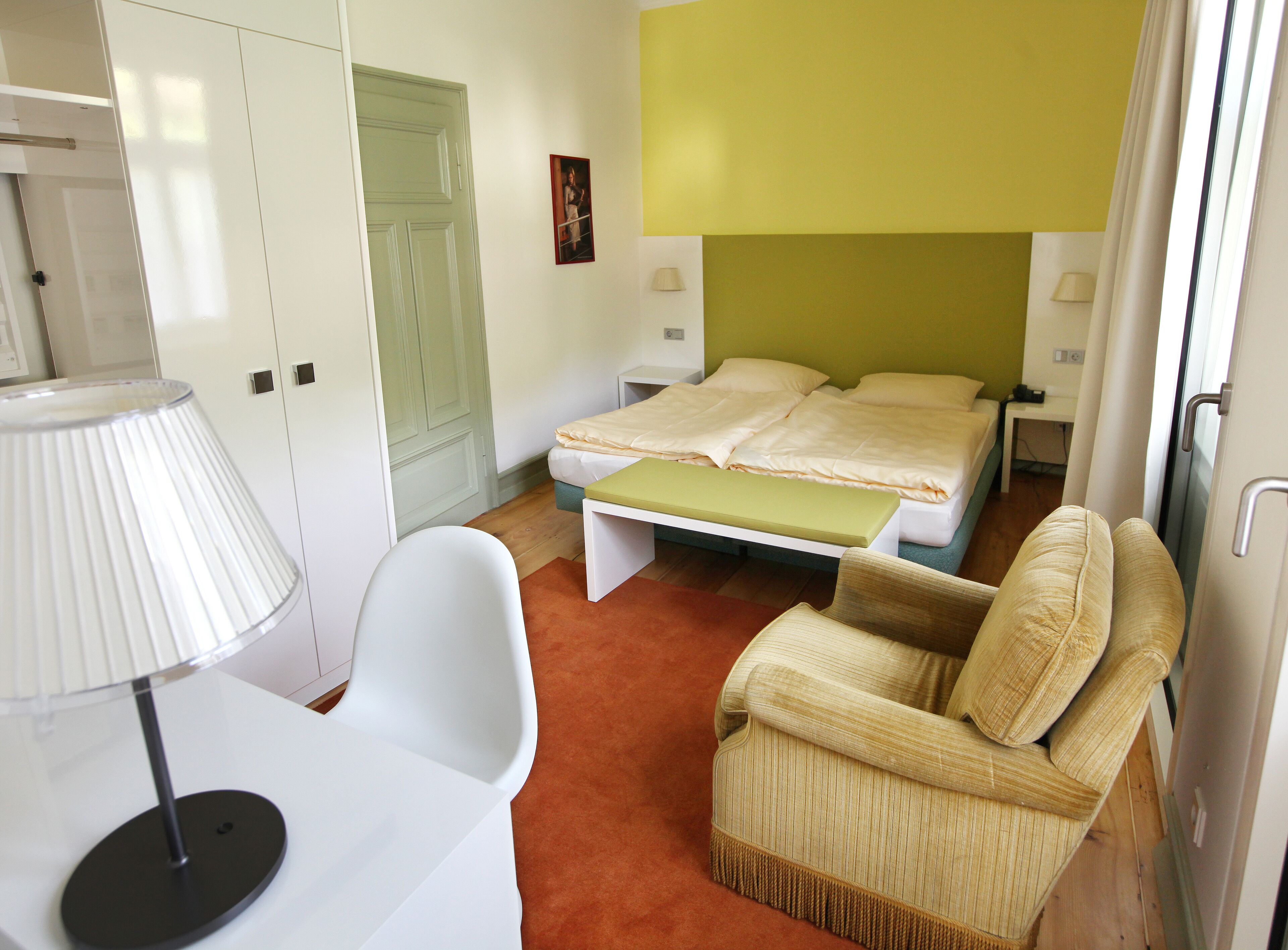 A bedroom with a bed, a chair, a desk, and a lamp.