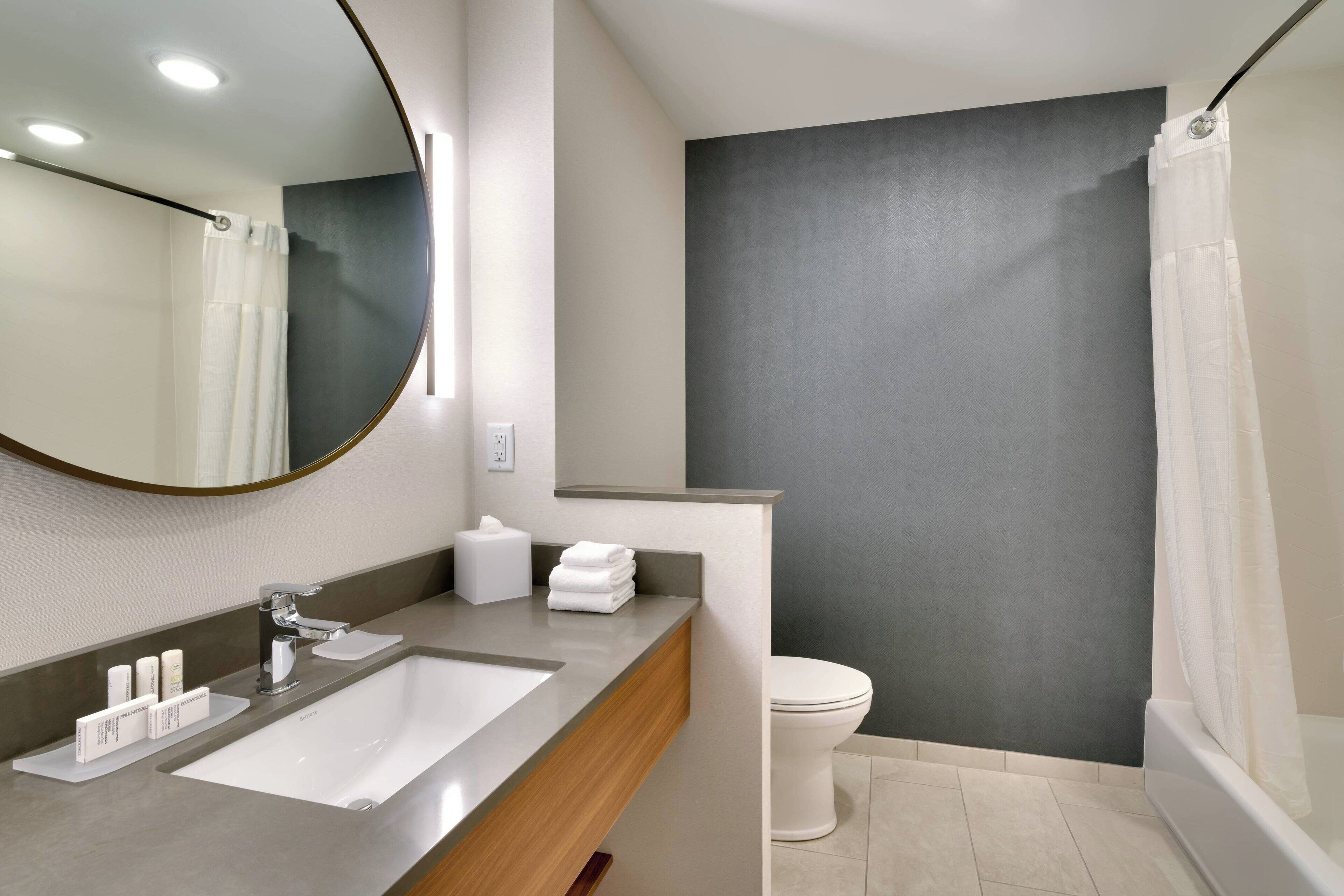 Un baño moderno con un espejo grande, un lavamanos, un inodoro y una zona de ducha.