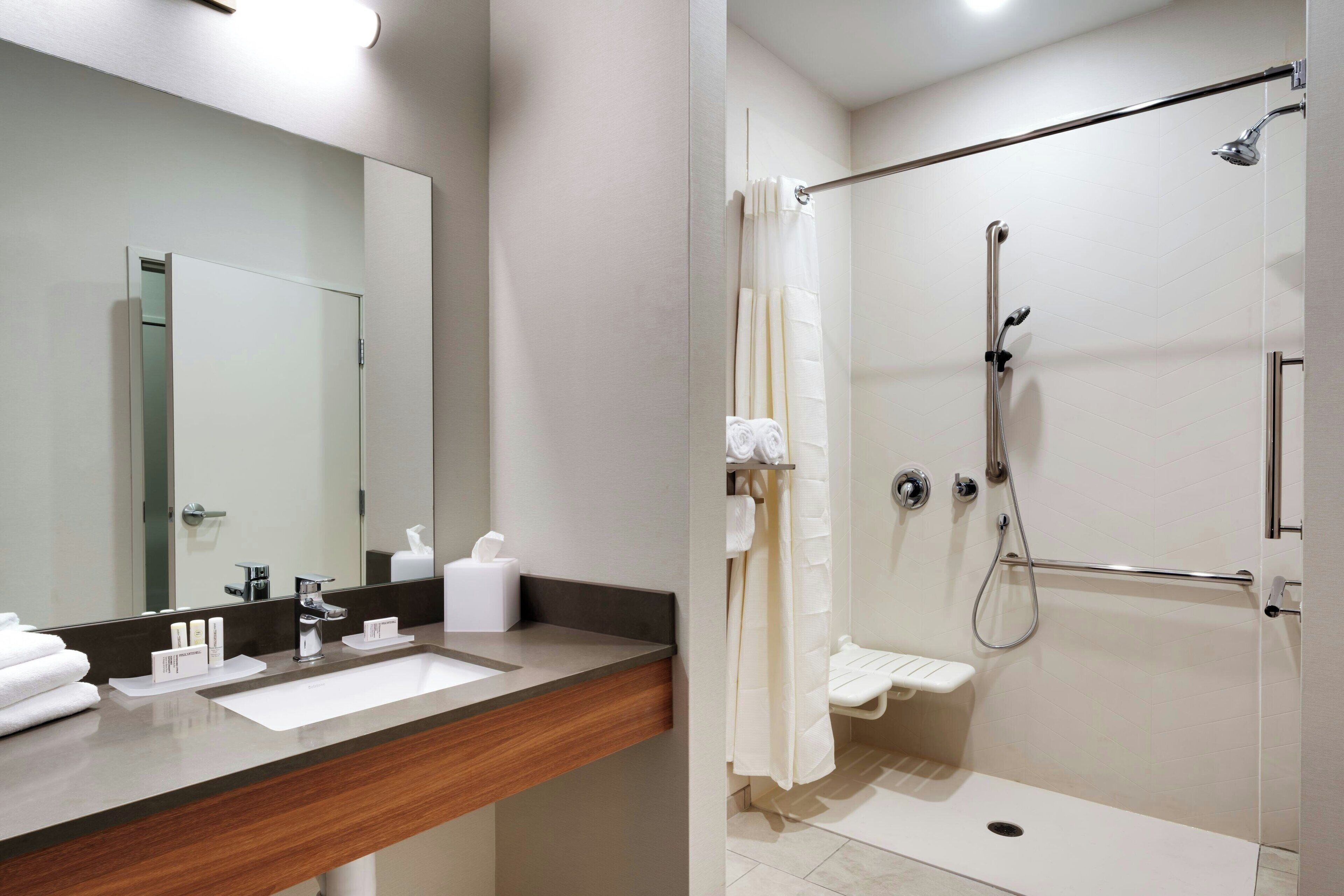 Une salle de bain moderne avec un meuble-lavabo en bois, un grand miroir, une douche avec une porte en verre et un porte-serviettes.
