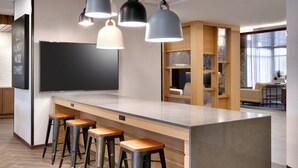 A modern kitchen area with bar stools, pendant lights, and a large flat-screen TV.