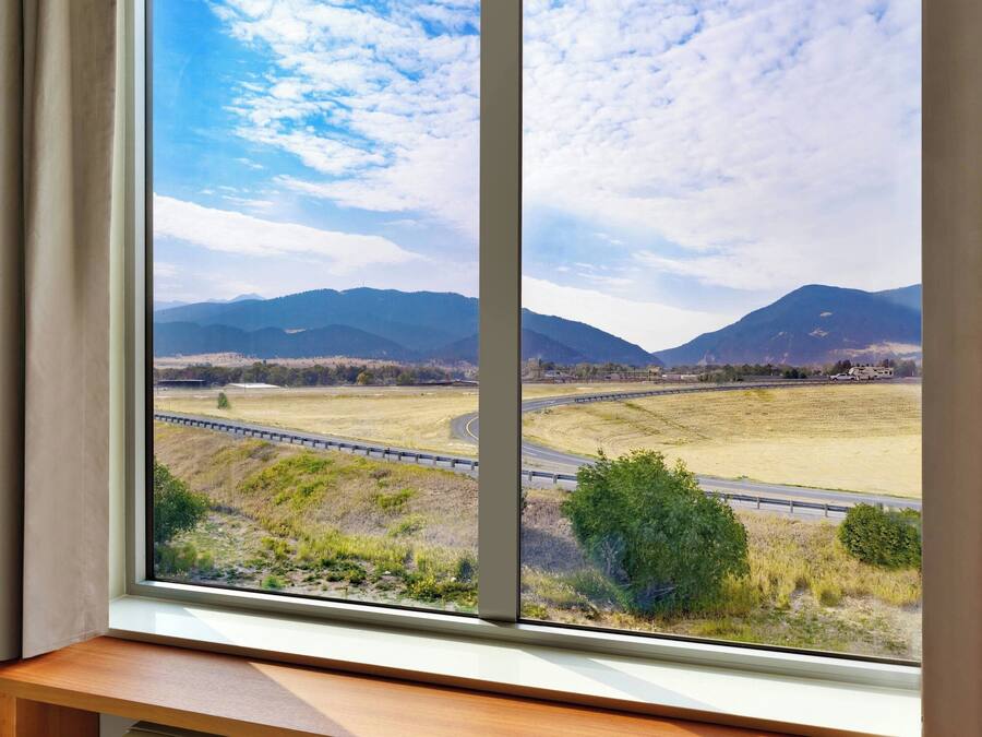 A view from a window with a view of a highway, mountains, and fields.