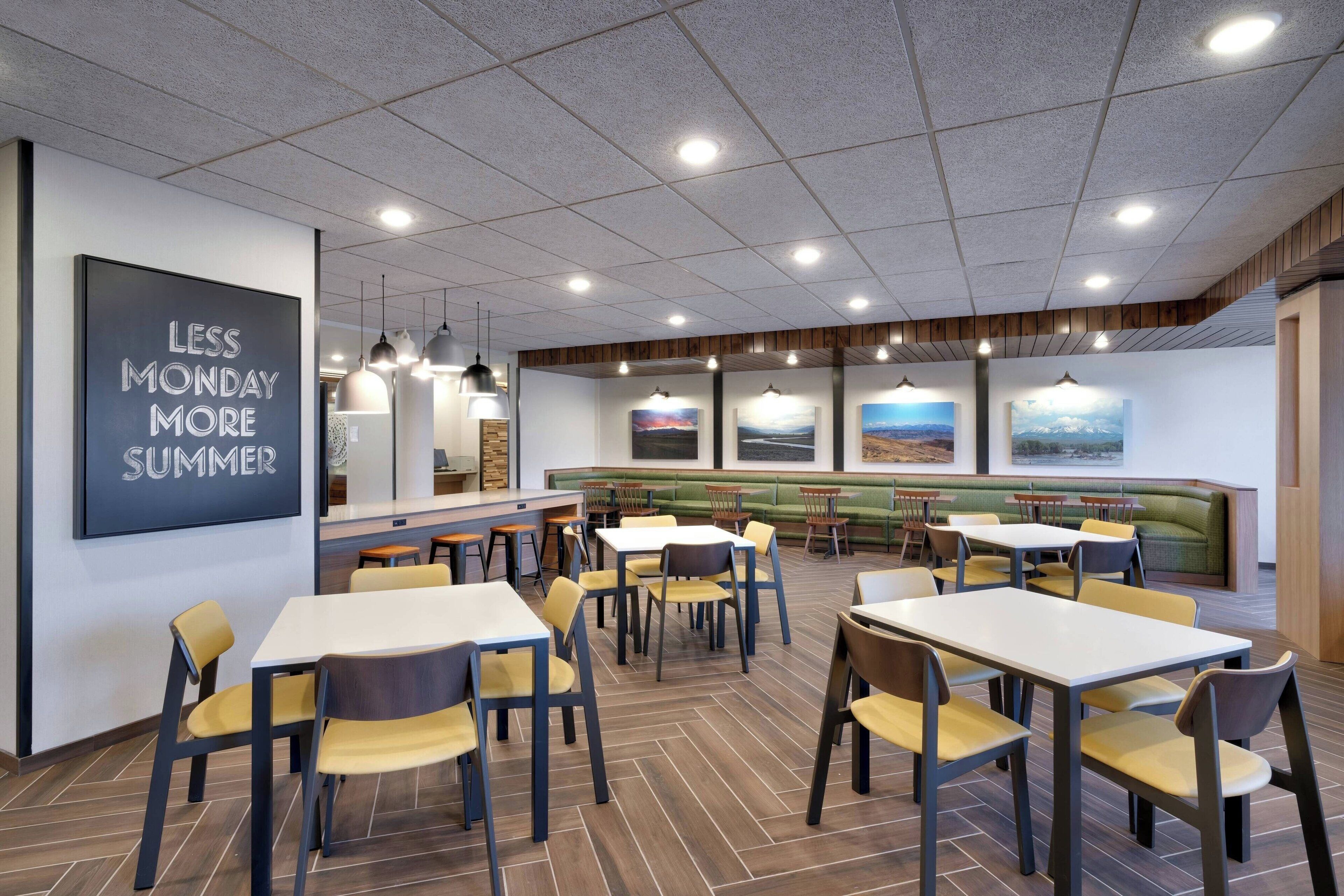 A modern dining area with tables and chairs, a wall with a motivational quote, and a seating area with a green couch and artwork.