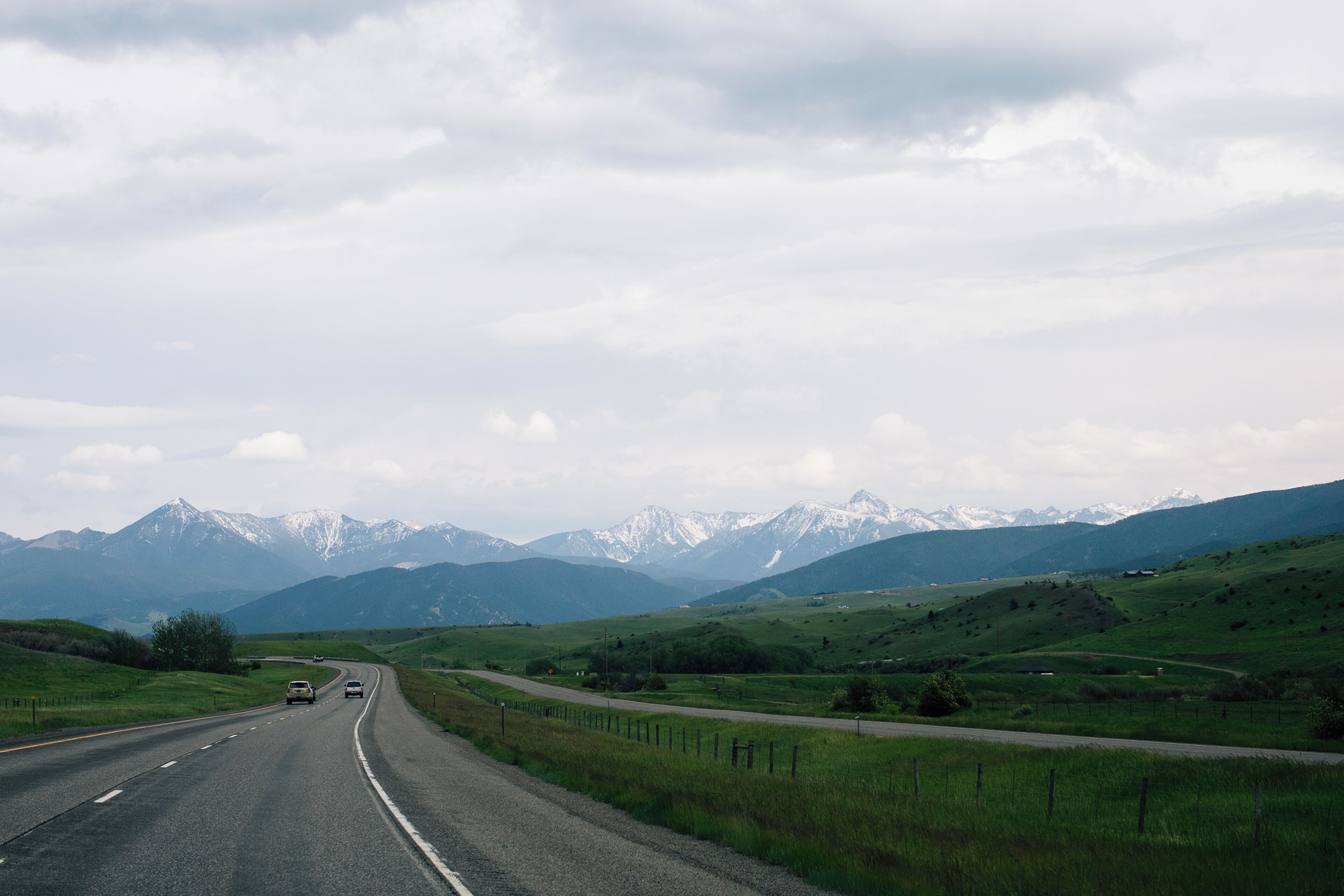 Une route bordée de véhicules, entourée de champs verdoyants et avec des montagnes qui se dessinent à l'horizon.
