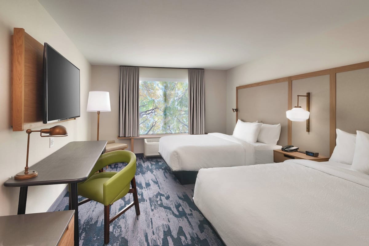 Hotelkamer met twee bedden, een bureau, een stoel, een televisie en een raam met gordijnen.