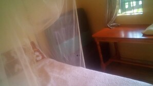 Una habitación con una cama cubierta por un dosel ligero, una mesa de madera y una ventana con cortinas.