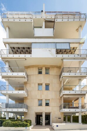 A multi-story building with balconies, a central entrance, and a clear sky.