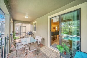 An outdoor patio with a glass table and chairs, a barbecue grill, and a view of a swimming pool through a glass door. - Family Fun & Secluded Pool! Gated Resort Near Disney (Davenport)
