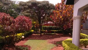A landscaped garden with a variety of shrubs and trees, a paved pathway, and outdoor seating. - EL Paso Gardens Kisumu (Kisumu)