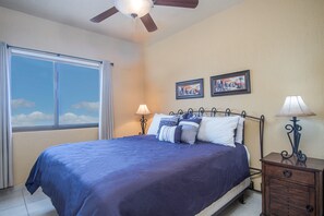 A bedroom with a bed, two wall-mounted lamps, a ceiling fan, a nightstand, and two framed pictures on the wall.