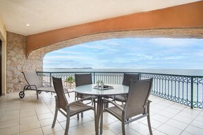 A balcony with a table and chairs, a view of the sea, and a stone wall.