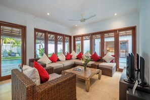 A spacious living area with wicker furniture, a coffee table, and a television. - 7-bedroom private estate in Seminyak, perfect for large groups and families. Accomodate up to 18 guests. Jasmina Estate includes daily breakfast, a private chef, airport transfers, complimentary massages, housekeeping, and a dedicated driver. (Seminyak)