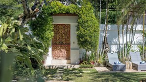A pool area with lounge chairs, a decorative door, and lush greenery. - 7-bedroom private estate in Seminyak, perfect for large groups and families. Accomodate up to 18 guests. Jasmina Estate includes daily breakfast, a private chef, airport transfers, complimentary massages, housekeeping, and a dedicated driver. (Seminyak)