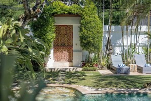 Un espace piscine agrémenté de chaises longues, d’une porte décorative et d’une végétation luxuriante.