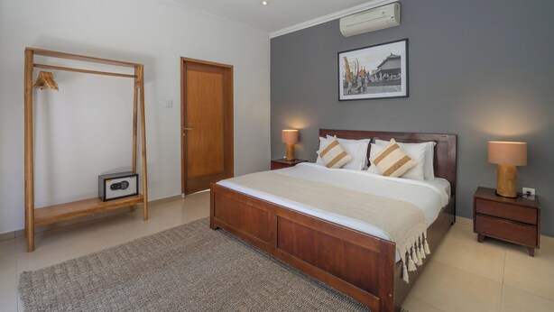 A bedroom with a wooden bed, bedside lamps, a framed picture on the wall, and a wooden wardrobe. - 7-bedroom private estate in Seminyak, perfect for large groups and families. Accomodate up to 18 guests. Jasmina Estate includes daily breakfast, a private chef, airport transfers, complimentary massages, housekeeping, and a dedicated driver. (Seminyak)