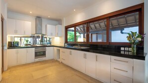 A modern kitchen with white cabinetry, stainless steel appliances, and a black countertop. - 7-bedroom private estate in Seminyak, perfect for large groups and families. Accomodate up to 18 guests. Jasmina Estate includes daily breakfast, a private chef, airport transfers, complimentary massages, housekeeping, and a dedicated driver. (Seminyak)