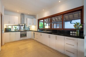 Une cuisine moderne avec des armoires blanches, une hotte de cuisinière en acier inoxydable et une grande fenêtre avec un cadre en bois.