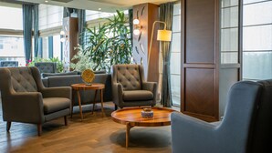 Un moderno vestíbulo de hotel con un área de descanso que incluye dos sillones y una mesa de centro redonda de madera.