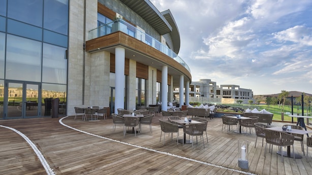 Un hotel moderno con terraza de madera, asientos al aire libre y vistas a un campo de golf.