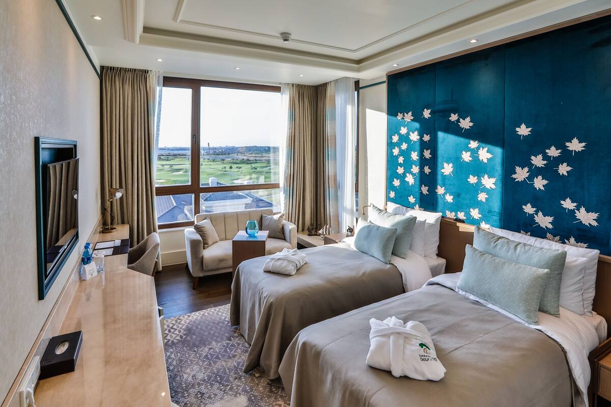 Ein Hotelzimmer mit zwei Betten, einem Fernseher, einem Schreibtisch und Blick auf einen Golfplatz.
