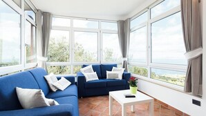 A sunlit room with two blue sofas, a white coffee table, and a view of greenery through large windows. - Villa Angela with private pool and sea view (Priora)