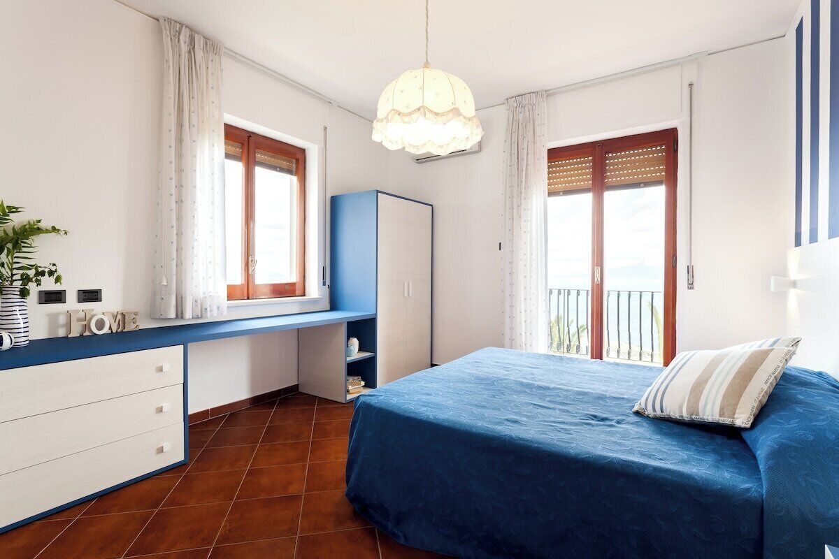 A bedroom with a bed, a desk, a wardrobe, and a balcony.